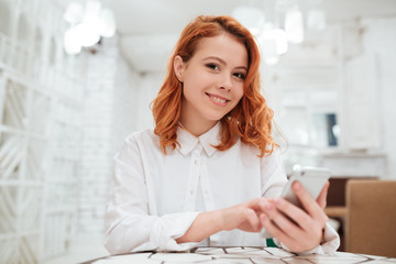 Pretty redhead young woman chatting while sitting in cafe