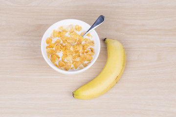 Cornflakes with milk and banana in the white bowl.
