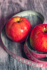 Two red apple with measuring tape on pink background. Healthy diet concept.