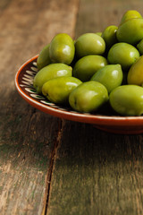 Green olives in brown bowl on wooden background. Close up. Copy space.