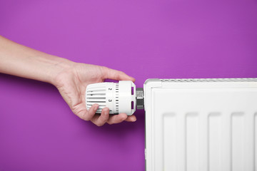 Female hand on temperature regulator of heating battery on pink background, closeup