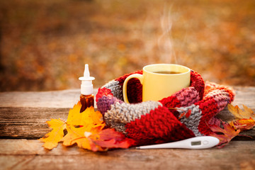 Tea mug and warm scarf with nose drops and fallen leaves