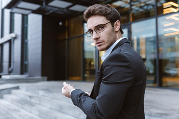 Business man in glasses standing sideways and looking at camera