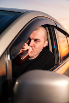 Young man drinking beer while driving car