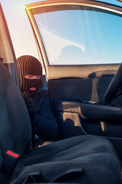 Male thief in robbery mask unlocking car door