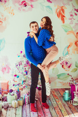 Strong man in blue sweater holds tiny lady on his arms standing