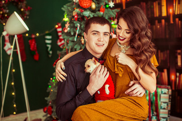 Fototapeta na wymiar Man hugs little dog sitting with his woman before Christmas tree