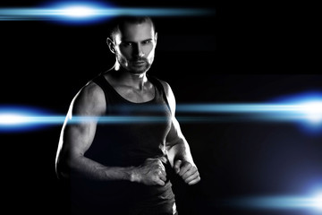 muscular man, clasps hands in fist, on the arena, around the glare of the spotlights