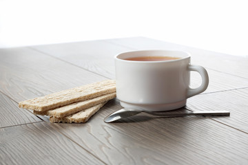 white cup of tea with biscuits and a teaspoon on a wooden table