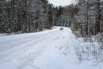 car traveling on snowy forest road between the trees