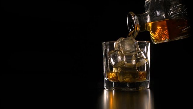 Whiskey on the rocks poured from a rystal decanter on black backround copy space