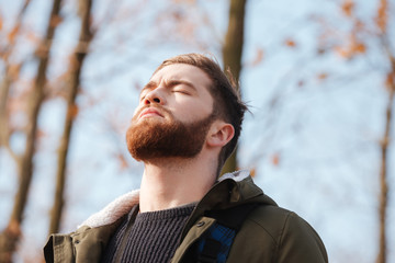 Relaxed bearded man standing in the forest with eyes closed.