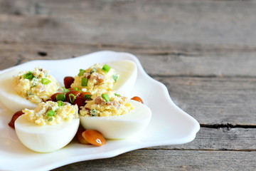 Basic stuffed eggs on a plate isolated on old wooden background with copy space for text. Hard-boiled eggs stuffed with cheese, mushrooms and green onions. Holiday appetizer recipe. Closeup
