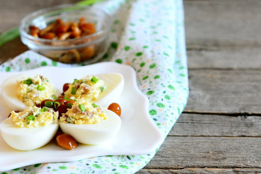 Tasty stuffed eggs on a plate, canned mushrooms in a bowl on old wooden table. Hard-boiled eggs stuffed with cheese, mushrooms and green onions. Easy and beautiful vegetarian snack. Closeup