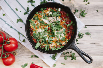 Delicious fresh morning Shakshuka on the wooden rustic table with some tomatoes on the side