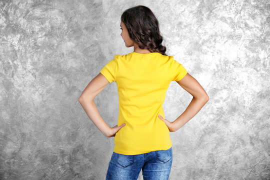 Young woman in blank yellow t-shirt standing against grey textured wall