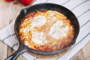 Delicious fresh morning Shakshuka on the wooden rustic table with some tomatoes on the side
