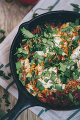 Delicious fresh morning Shakshuka on the wooden rustic table with some tomatoes on the side