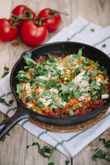 Delicious fresh morning Shakshuka on the wooden rustic table with some tomatoes on the side