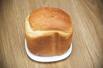 Loaf of white fresh bread on a plate on a wooden table