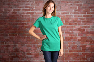 Young woman in blank green t-shirt standing against brick wall