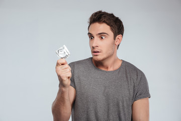 Portrait of an astonished young man looking at condom
