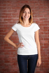 Young woman in blank white t-shirt standing against brick wall