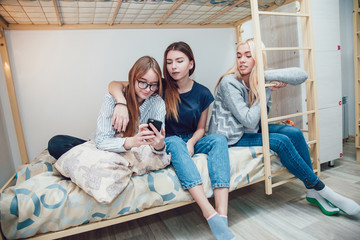 Beautiful girls sitting on a bed in hostel talk and using smartphone.