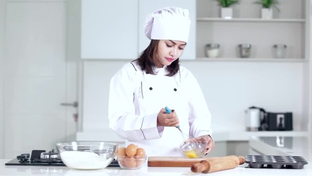 
Beautiful woman cooking cake in the kitchen while whisking egg on a bowl and wearing uniform
