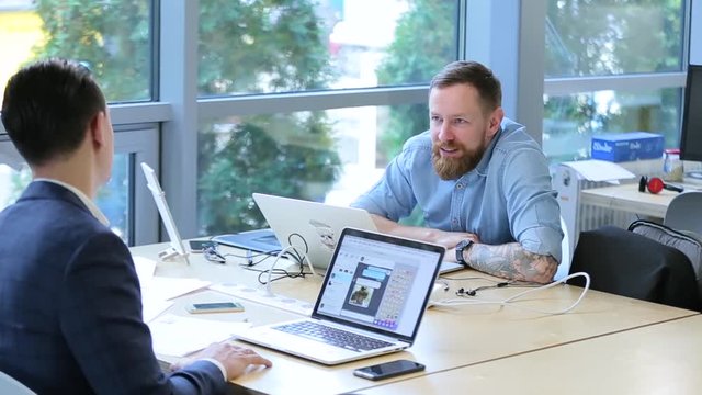 business men talking in an office with laptops.
