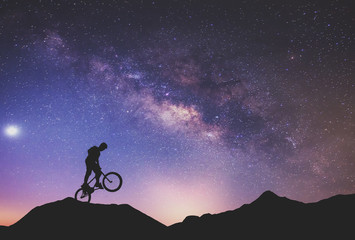Man riding a bike performing a trick against on Mountain with Milky way.