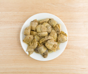 Marinated artichoke hearts on a plate atop a wood table top view.