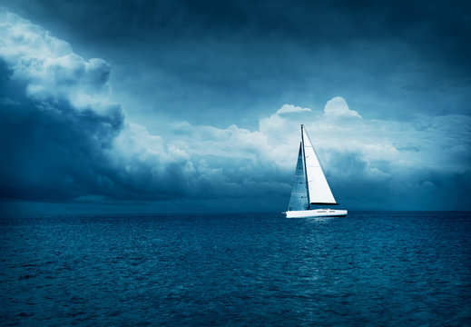 White Yacht Sailing In Stormy Sea. Dark Thundery Night Background. Dramatic Storm Cloudscape. Danger In Sea Concept. Cold Toned Photo With Copy Space.