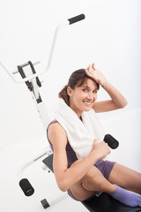 femme souriant sportive qui transpire assise sur un banc de musculation 