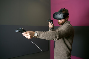 bearded man using the virtual reality glasses and two gamepad