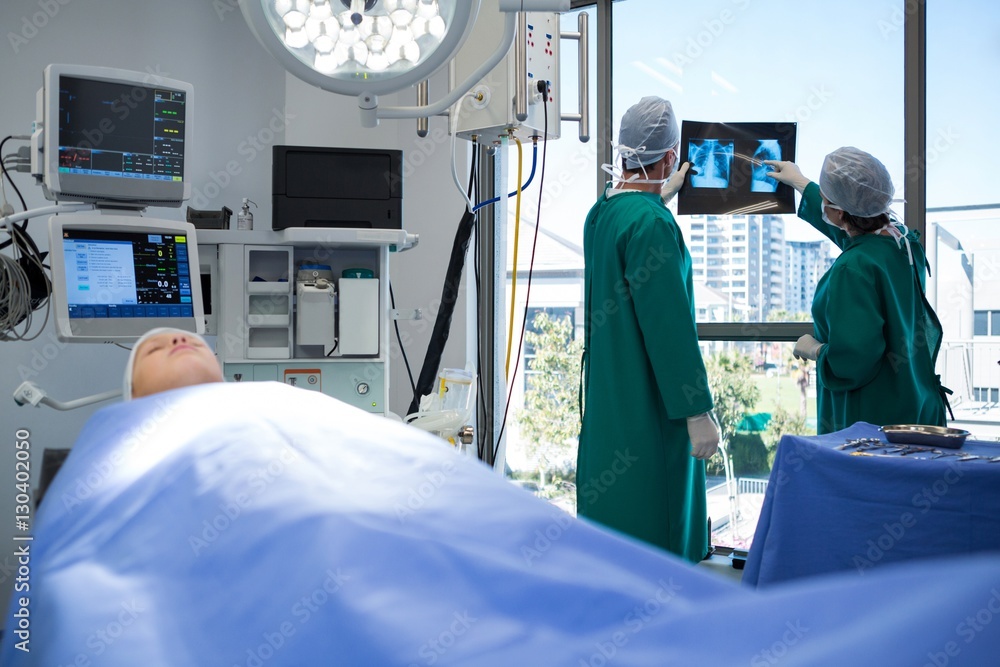 Poster surgeons discussing x-ray while operating patient