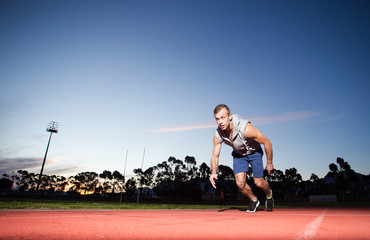 Male sprinter athlete on a tartan athletic track getting ready f
