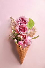 Waffle cone with composition of flowers and branches on pink background