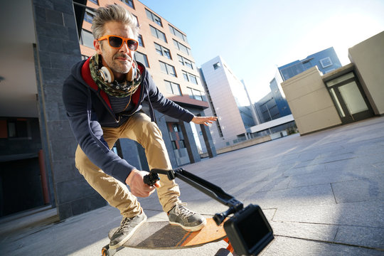 Mature man skateboarding in urban environment, filming himself