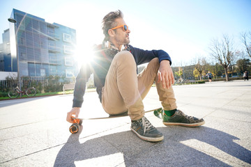 Trendy urban guy sitting on skateboard in park