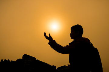 Silhouette of man kneeling and praying over beautiful sunrise on mountain background
