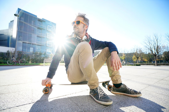 Trendy urban guy sitting on skateboard in park