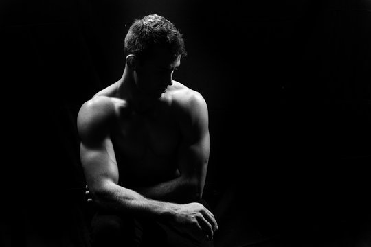 Male fitness model showing muscles in studio with a black backgr