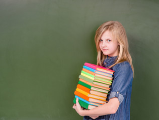 Girl with a pile books near empty green chalkboard