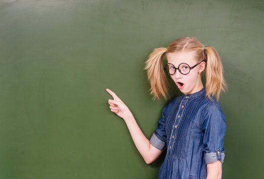Shocked girl points on empty green chalkboard