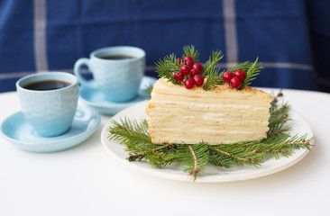 cake decorated Christmas tree branches and berries on a background of the Christmas tree and two cups of coffee