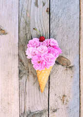 Flowers composition - pink roses flowers and cherry in ice cream cone on rustic wooden background. Stylish flat lay. Minimal and spring concept.