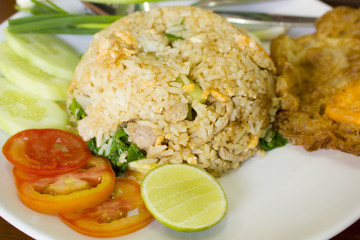 fried rice with fried egg on white dish with tomatoes cucumber and lime slice