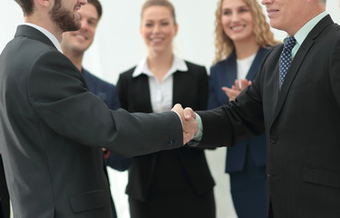 Mature businessman shaking hand of  his partner with colleagues 