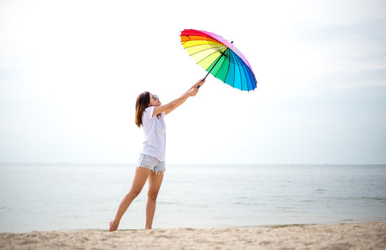 Young women jumping with umbella and happy on the beach. Travel and Vacation. Freedom Concept